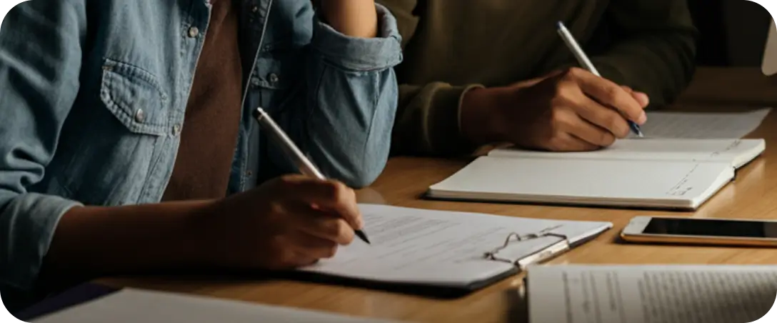 Two students taking notes in a notebook with a pen